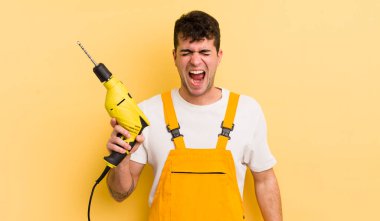 Genç yakışıklı adam agresif bir şekilde bağırıyor, çok kızgın görünüyor. Tamirci ve matkap konsepti