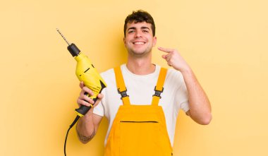 Genç ve yakışıklı bir adam kendi gülüşünü işaret ederek kendine güvenerek gülümsüyor. Tamirci ve matkap konsepti