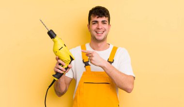 Genç yakışıklı adam heyecanlı ve şaşırmış görünüyor. Tamirci ve matkap konsepti