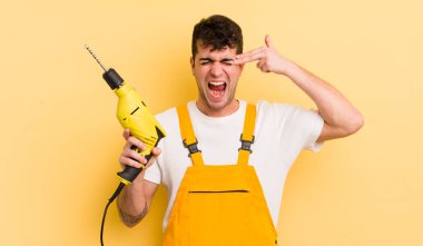 Genç yakışıklı adam mutsuz ve stresli görünüyor, intihar jesti silah işareti yapıyor. Tamirci ve matkap konsepti