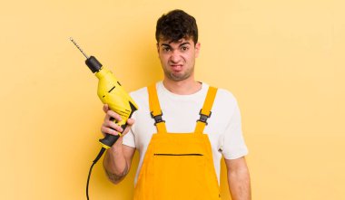 Genç yakışıklı adam şaşkın ve şaşkın hissediyor. Tamirci ve matkap konsepti