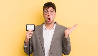 Genç, yakışıklı adam şaşırmış ve şok olmuş görünüyor. Çenesi düşmüş, elinde bir nesne var. VIP geçiş konsepti