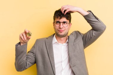 Kafası karışmış, kafası karışmış, kaşınan genç, yakışıklı bir adam. Bitcoin konsepti