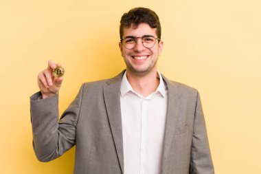 Genç yakışıklı adam mutlu bir şekilde gülümsüyor, eli kalçasında ve kendinden emin. Bitcoin konsepti