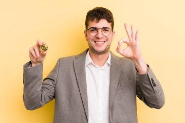 Genç yakışıklı adam kendini mutlu hissediyor, iyi bir jestle onaylıyor. Bitcoin konsepti