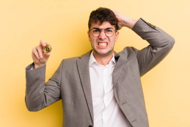 Genç ve yakışıklı bir adam stresli, endişeli ya da korkmuş hissediyor. Elleri başının üstünde. Bitcoin konsepti