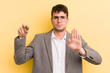 Genç ve yakışıklı adam ciddi görünüyor. Avuç içi gösteriyor. Durdurma hareketi yapıyor. Bitcoin konsepti