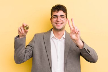 Genç yakışıklı adam gülümsüyor ve mutlu görünüyor, zafer ya da barış işareti yapıyor. Bitcoin konsepti