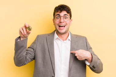 Genç ve yakışıklı bir adam mutlu hissediyor ve heyecanla kendini işaret ediyor. Bitcoin konsepti
