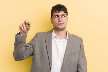 Genç yakışıklı adam omuz silkiyor, kafası karışık ve kararsız. Bitcoin konsepti