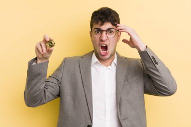 Genç yakışıklı adam kafası karışık ve şaşkın hissediyor, deli olduğunu gösteriyor. Bitcoin konsepti