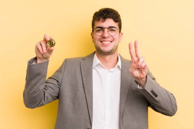 Genç yakışıklı adam gülümsüyor ve arkadaş canlısı görünüyor, iki numarayı gösteriyor. Bitcoin konsepti