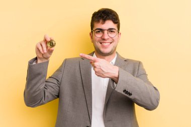 Genç yakışıklı adam neşeyle gülümsüyor, mutlu hissediyor ve bir tarafı işaret ediyor. Bitcoin konsepti