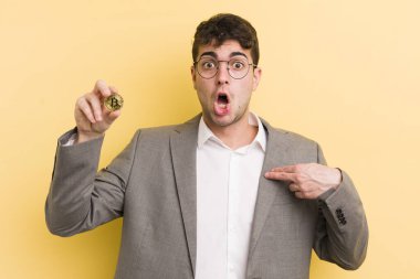 Şok olmuş ve ağzı açık, kendini işaret eden genç ve yakışıklı bir adam. Bitcoin konsepti