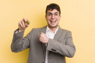 Genç yakışıklı adam kendini mutlu hissediyor ve bir meydan okumayla yüzleşiyor ya da kutluyor. Bitcoin konsepti