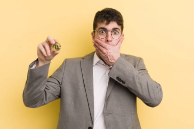 Genç ve yakışıklı bir adam elleri ile ağzını kapatıyor ve şok geçiriyor. Bitcoin konsepti