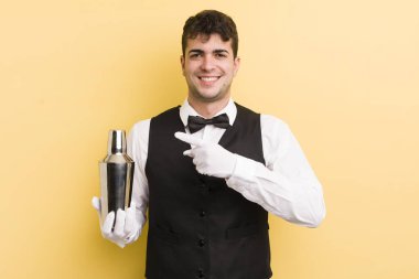 Genç yakışıklı adam neşeyle gülümsüyor, mutlu hissediyor ve bir tarafı işaret ediyor. barmen kokteyli