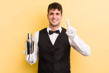 Genç yakışıklı adam gülümsüyor ve arkadaş canlısı görünüyor, bir numarayı gösteriyor. barmen kokteyli