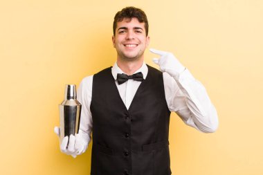 Genç ve yakışıklı bir adam kendi gülüşünü işaret ederek kendine güvenerek gülümsüyor. barmen kokteyli