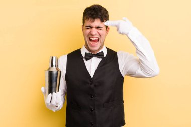 Genç yakışıklı adam mutsuz ve stresli görünüyor, intihar jesti silah işareti yapıyor. barmen kokteyli