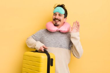 Genç yakışıklı adam mutlu bir şekilde gülümsüyor, el sallıyor, sizi selamlıyor ve selamlıyor. seyahat yolcu kavramı