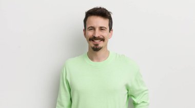 Genç yakışıklı adam mutlu bir şekilde gülümsüyor, eli kalçasında ve kendinden emin.