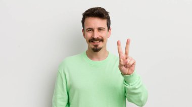 Genç yakışıklı adam gülümsüyor ve mutlu görünüyor, zafer ya da barış işareti yapıyor.