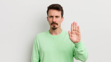 Genç ve yakışıklı adam ciddi görünüyor. Avuç içi gösteriyor. Durdurma hareketi yapıyor.
