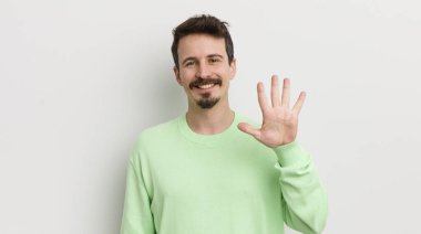 Genç yakışıklı adam gülümsüyor ve arkadaş canlısı görünüyor, beş numarayı gösteriyor.