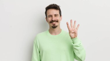Genç yakışıklı adam gülümsüyor ve arkadaş canlısı görünüyor, dört numarayı gösteriyor.