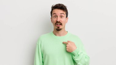 Şok olmuş ve ağzı açık, kendini işaret eden genç yakışıklı bir adam.