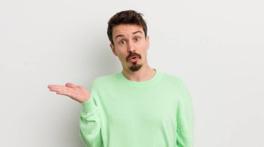 Genç yakışıklı adam şaşırmış ve şok olmuş görünüyor, çenesi düşmüş bir nesne tutuyor.