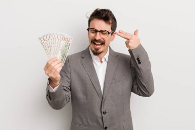Genç yakışıklı adam mutsuz ve stresli görünüyor, intihar jesti silah işareti yapıyor. İş adamı ve banknotlar