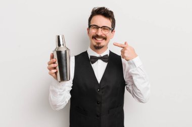 Genç ve yakışıklı bir adam kendi gülüşünü işaret ederek kendine güvenerek gülümsüyor. Kokteyl barmeni