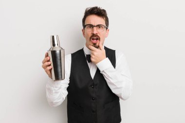 Ağzı ve gözleri açık ve eli çenesinde genç yakışıklı bir adam. Kokteyl barmeni