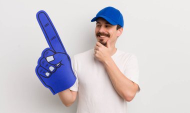 Genç ve yakışıklı bir adam mutlu ve kendinden emin bir ifadeyle gülümsüyor, elleri çenesinde. Bir numaralı el konsepti