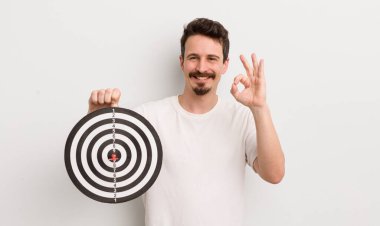 Genç yakışıklı adam kendini mutlu hissediyor, iyi bir jestle onaylıyor. dart hedef konsepti