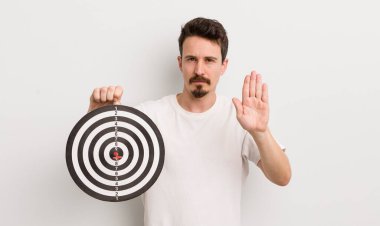 Genç ve yakışıklı adam ciddi görünüyor. Avuç içi gösteriyor. Durdurma hareketi yapıyor. dart hedef konsepti