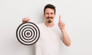 Genç yakışıklı adam gülümsüyor ve arkadaş canlısı görünüyor, bir numarayı gösteriyor. dart hedef konsepti
