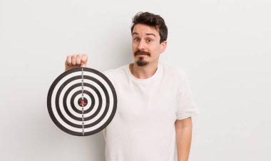 Genç yakışıklı adam omuz silkiyor, kafası karışık ve kararsız. dart hedef konsepti