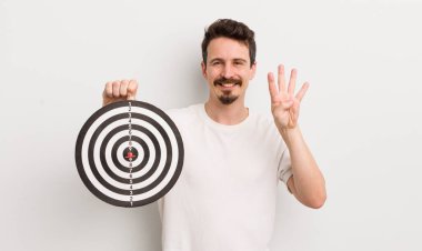 Genç yakışıklı adam gülümsüyor ve arkadaş canlısı görünüyor, dört numarayı gösteriyor. dart hedef konsepti