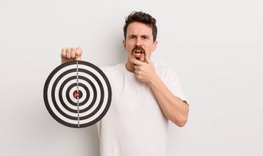 Ağzı ve gözleri açık ve eli çenesinde genç yakışıklı bir adam. dart hedef konsepti