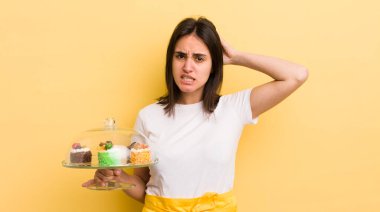 Genç İspanyol kadın stresli, endişeli ya da korkmuş hissediyor, elleri başının üstünde. Ev yapımı kek konsepti