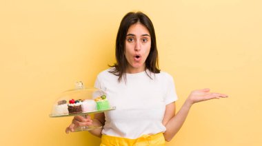 Genç İspanyol kadın şaşırmış ve şok olmuş görünüyor. Çenesi düşmüş ve elinde bir nesne tutuyor. Ev yapımı kek konsepti