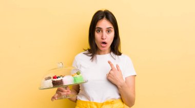 Genç İspanyol kadın şok olmuş ve ağzı açık, kendini işaret ederek şaşırmış görünüyor. Ev yapımı kek konsepti