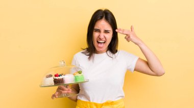 Genç İspanyol kadın mutsuz ve stresli görünüyor, intihar jesti silah işareti yapıyor. Ev yapımı kek konsepti