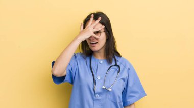 Genç İspanyol bir kadın şok olmuş, korkmuş ya da korkmuş görünüyor. Yüzü elle kapatılmış. hemşire konsepti