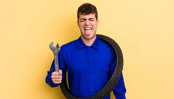 陽気で反抗的な態度を持つ若いハンサムな男冗談と舌を突き出す 自転車修理工のコンセプト — ストック写真