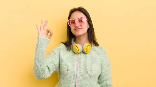 若いヒスパニック系の女性は幸せを感じます 大丈夫なジェスチャーで承認を示し ヘッドフォンとサングラスのコンセプト — ストック写真
