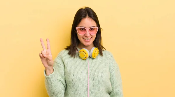 若いヒスパニック系の女性の笑顔と友好的に見える 2番目を示す ヘッドフォンとサングラスのコンセプト — ストック写真